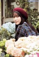 A woman wearing a red beret standing in front of flowers.