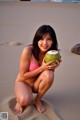 A woman in a pink bikini holding a coconut on the beach.