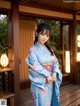 A woman in a blue kimono standing on a wooden deck.