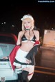 A woman in a maid outfit standing next to a car.