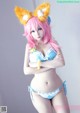 A woman in a blue bikini with pink hair and fox ears.