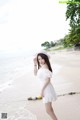 A woman in a white dress and hat standing on a beach.