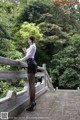 A woman in a white shirt and black skirt standing on a bridge.