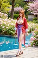 A woman in a traditional red and purple kimono stands by a pool surrounded by blooming flowers.