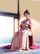 A woman in a pink and white kimono sitting on a chair.