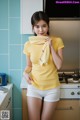 A woman in a yellow shirt and white shorts standing in a kitchen.