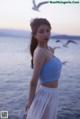 A woman in a blue top and white skirt standing by the water.