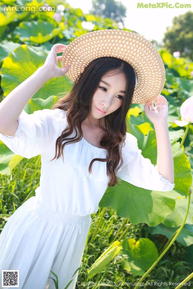 A woman in a white dress and straw hat standing in a field of flowers.